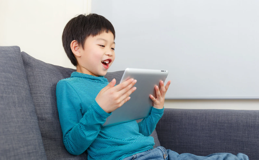 Young preschool child smiling while holding a tablet, enjoying the benefits of educational games, apps and videos, such as improved motor skills, better academic performance and literary skills