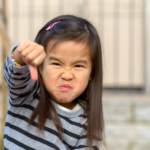 Preschool child throwing a temper tantrum with a frowning face and making a thumbs down sign